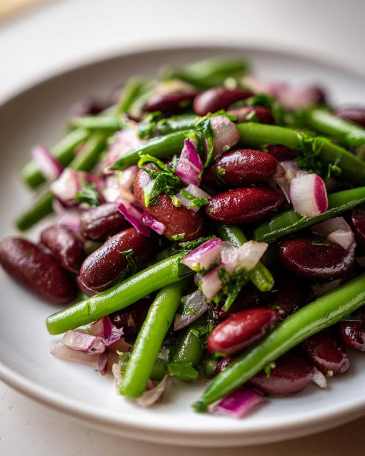 Close-up of a fresh bean salad featuring dark red kidney beans, bright green beans, and chopped red onion.
