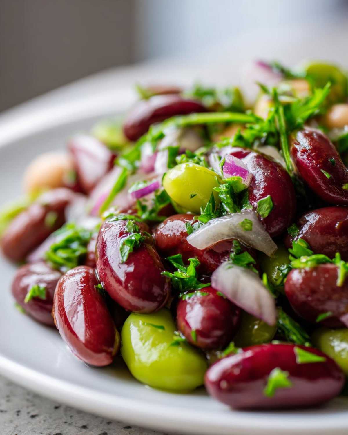 Close-up of a vibrant mixed bean salad featuring kidney beans, green beans, red onion, and parsley.