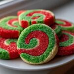 A stack of festive red and green pinwheel cookies coated in sparkling sugar on a white plate.