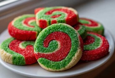 A stack of festive red and green pinwheel cookies coated in sparkling sugar on a white plate.