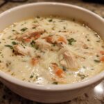 Close-up of a bowl of creamy white chicken lasagna soup topped with shredded cheese and parsley.