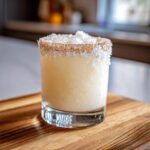 A frosty white Christmas margarita cocktail with a toasted coconut rim, served in a rocks glass.
