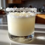 Close-up of a frosty white Christmas margarita in a rocks glass with a thick, snowy salt rim.