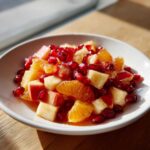 Close-up of a vibrant winter fruit salad featuring diced apples, orange segments, and bright pomegranate seeds.