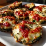 Close-up of several baked zucchini pizza bites topped with melted mozzarella, marinara sauce, and herbs.