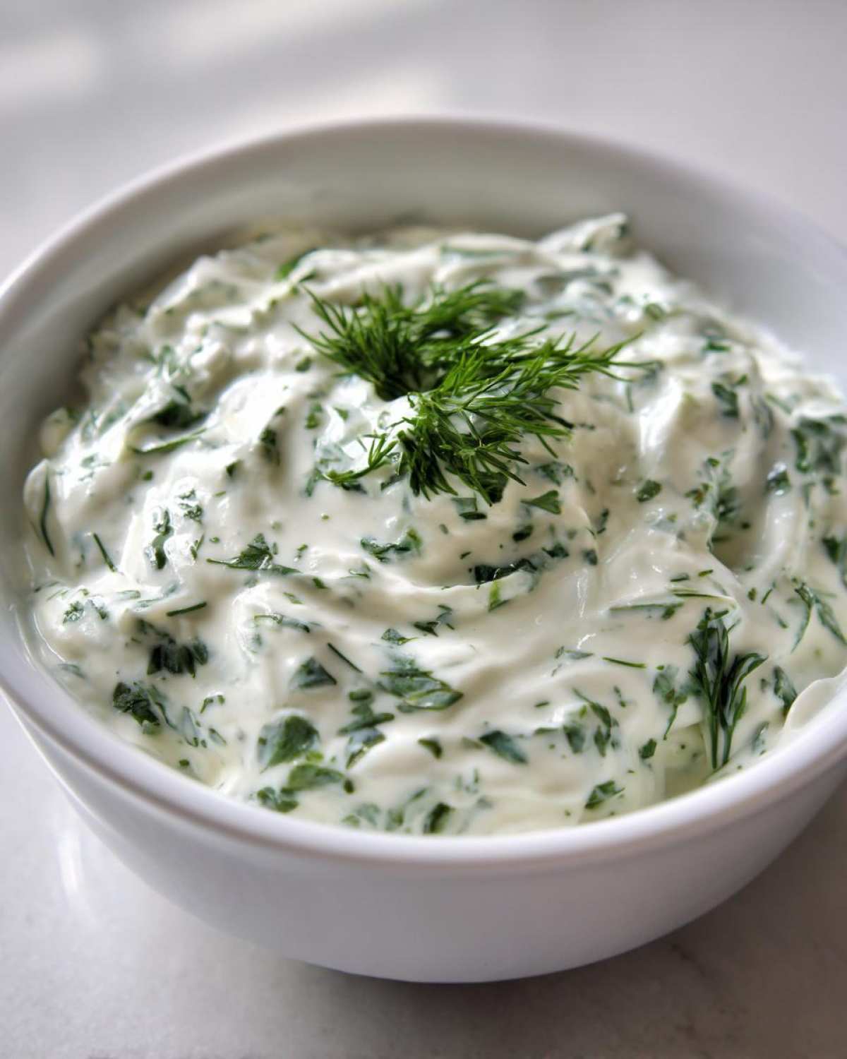 Close-up of creamy 5-Minute Greek Yogurt Ranch Dip mixed with fresh green herbs and topped with dill.