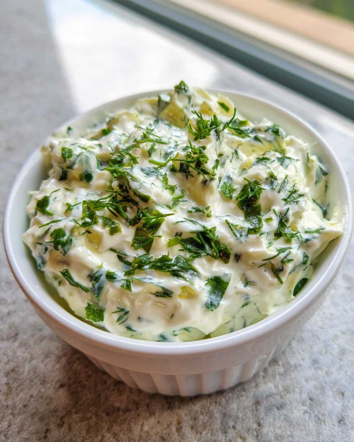 A close-up of thick, creamy 5-Minute Greek Yogurt Ranch Dip topped generously with fresh chopped green herbs.