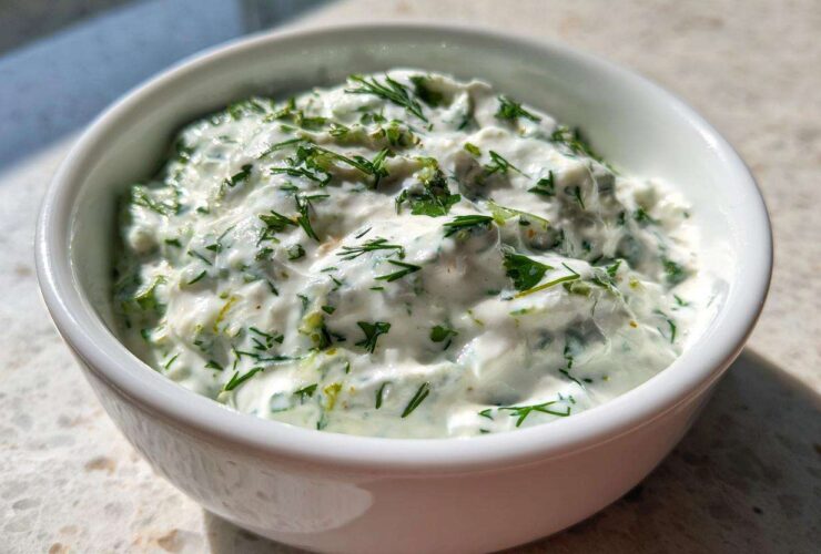 A white bowl filled with thick, creamy 5-Minute Greek Yogurt Ranch Dip, heavily speckled with fresh green herbs like dill and parsley.