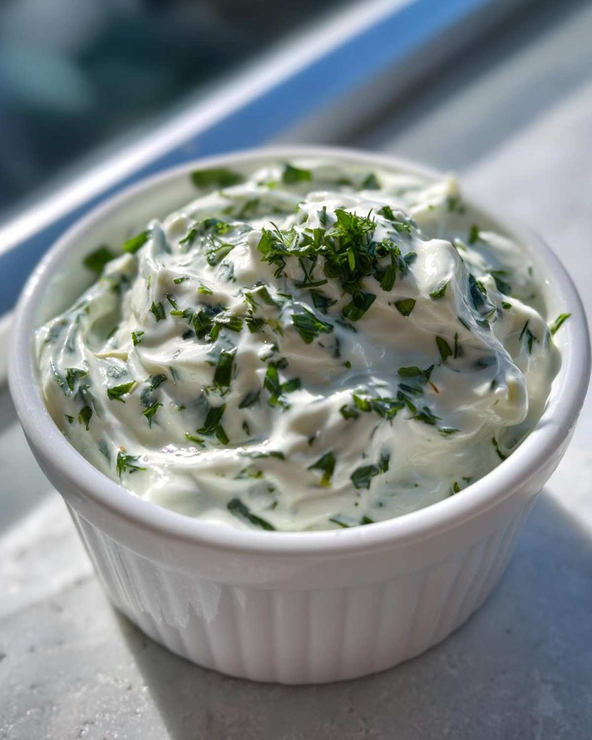 A close-up of thick, creamy 5-Minute Greek Yogurt Ranch Dip topped with fresh chopped green herbs in a white ramekin.