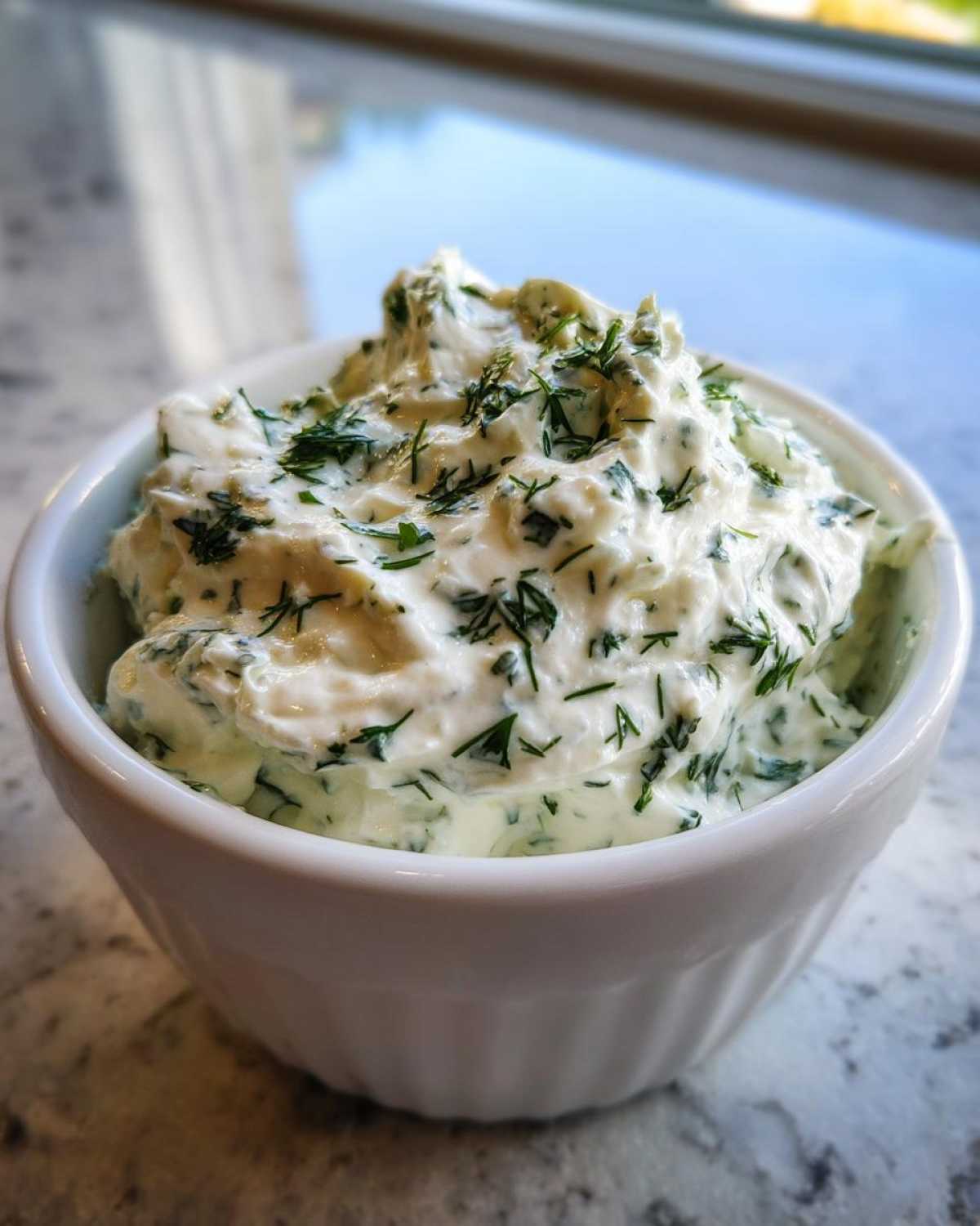 Close-up of thick, creamy 5-Minute Greek Yogurt Ranch Dip topped generously with fresh chopped dill in a white ramekin.