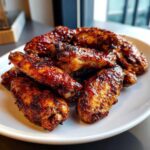 Close-up of crispy, glazed Air Fryer BBQ Chicken Wings piled high on a white plate.