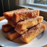 A stack of golden brown Air Fryer French Toast Sticks heavily coated in cinnamon sugar on a white plate.