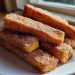 A stack of golden brown Air Fryer French Toast Sticks heavily coated in sparkling cinnamon sugar on a white plate.