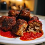 Close-up of several browned Air Fryer Italian Meatballs resting in bright red marinara sauce on a white plate.