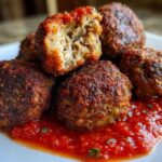 Close-up of perfectly browned Air Fryer Italian Meatballs served on a white plate with a pool of bright red marinara sauce.