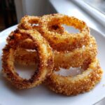 Close-up of four golden brown, crispy Air Fryer Onion Rings stacked on a white plate.