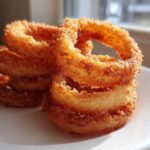 A stack of perfectly golden, crispy Air Fryer Onion Rings resting on a white plate near a window.