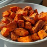 A white bowl filled with perfectly seasoned and browned Air Fryer Sweet Potato Cubes, catching bright sunlight.