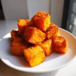 A close-up stack of golden brown, crispy Air Fryer Sweet Potato Cubes served on a small white plate.