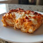 A close-up of a square serving of Baked Buffalo Chicken Dip showing shredded chicken texture and melted, browned cheese topping.