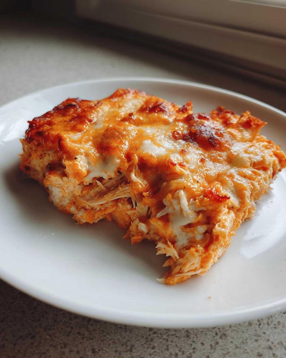 A close-up shot of a hearty serving of Baked Buffalo Chicken Dip topped with bubbly, browned cheese on a white plate.