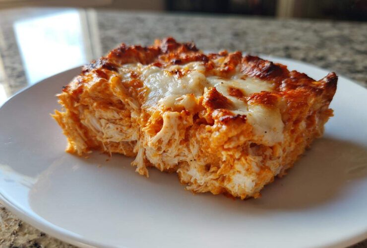A close-up of a square serving of Baked Buffalo Chicken Dip showing shredded chicken texture and melted, browned cheese topping.