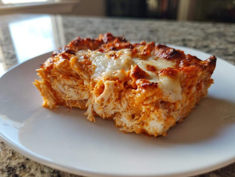 A close-up of a square serving of Baked Buffalo Chicken Dip showing shredded chicken texture and melted, browned cheese topping.