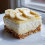 A close-up of a rich Banana Pudding Cheesecake Bars square with a graham cracker crust, creamy filling, and fresh banana slices on top.