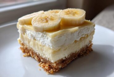 A single serving of Banana Pudding Cheesecake Bars featuring a graham cracker crust, creamy filling, whipped topping, and fresh banana slices.