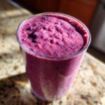 A close-up of a thick, vibrant purple Blueberry Lemon Chia Smoothie served in a clear glass on a granite counter.