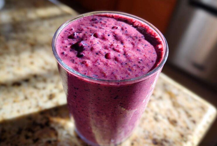A close-up of a thick, vibrant purple Blueberry Lemon Chia Smoothie served in a clear glass on a granite counter.