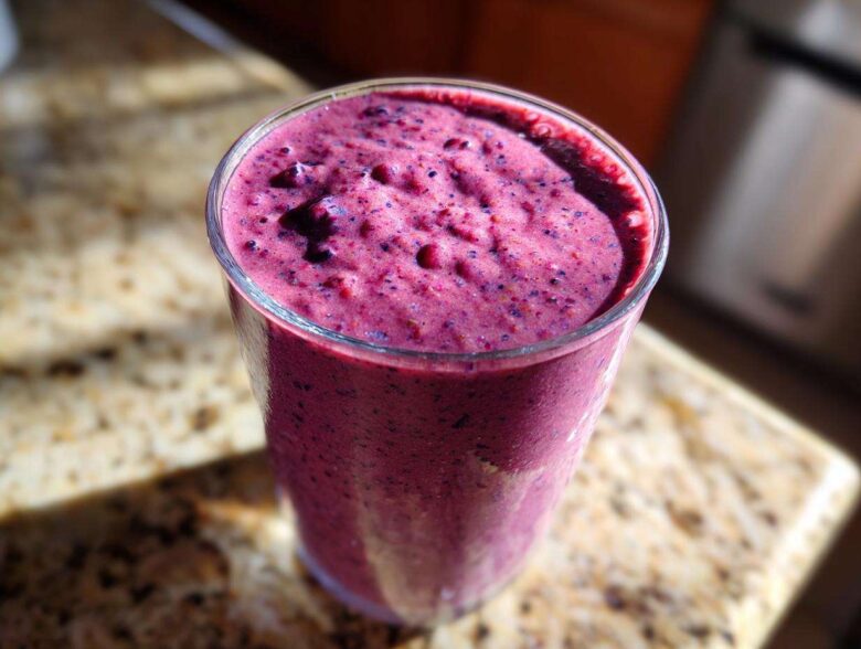 A close-up of a thick, vibrant purple Blueberry Lemon Chia Smoothie served in a clear glass on a granite counter.