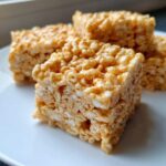 Close-up of several gooey Brown Butter Rice Krispie Treat Bars stacked slightly on a white plate.
