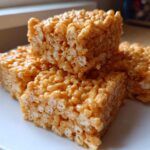 Four golden-brown squares of gooey Brown Butter Rice Krispie Treat Bars stacked slightly on a white plate.