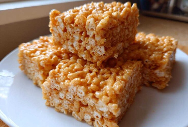 Four golden-brown squares of gooey Brown Butter Rice Krispie Treat Bars stacked slightly on a white plate.