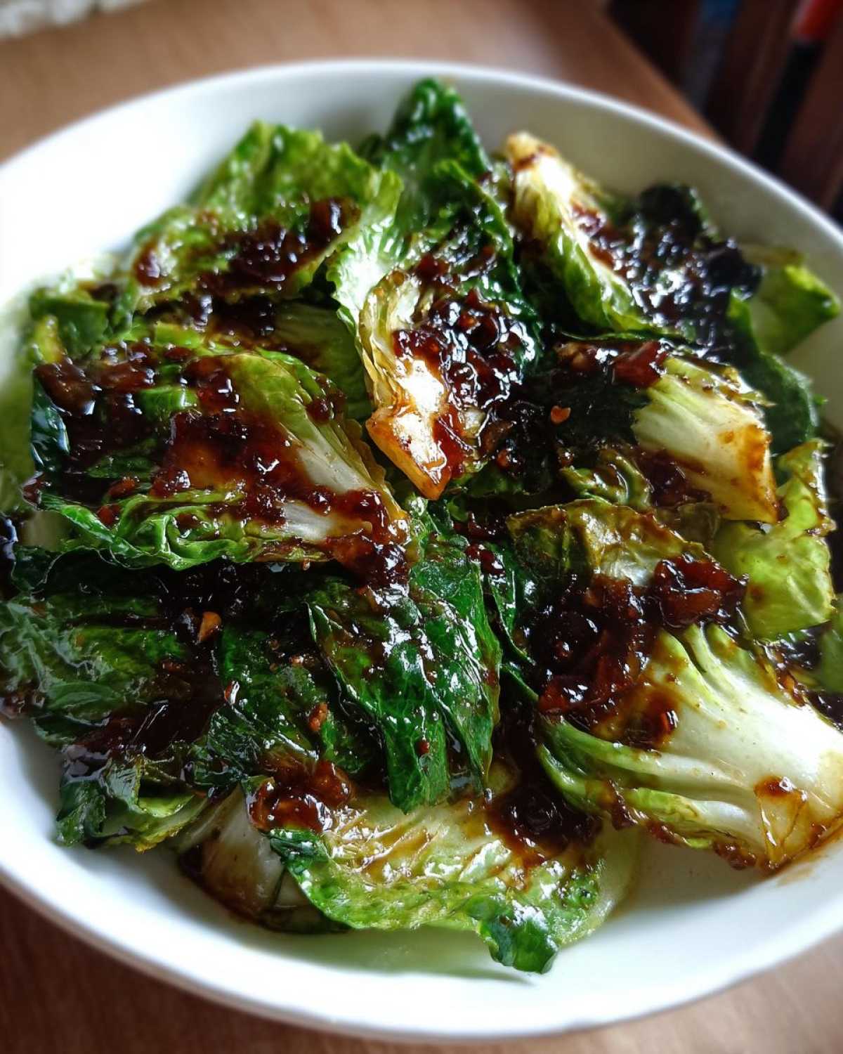 Close-up of wilted green cabbage pieces coated in a rich, dark Garlic Ginger Sauce, part of the Cabbage Stir Fry.