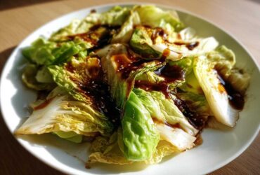 Close-up of Cabbage Stir Fry with Garlic Ginger Sauce, featuring wilted cabbage drizzled with dark sauce and sesame seeds.