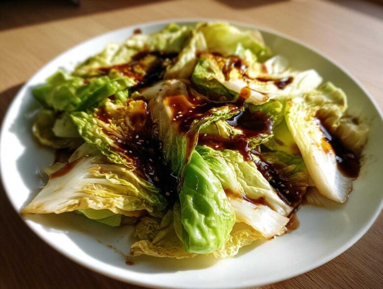 Close-up of Cabbage Stir Fry with Garlic Ginger Sauce, featuring wilted cabbage drizzled with dark sauce and sesame seeds.