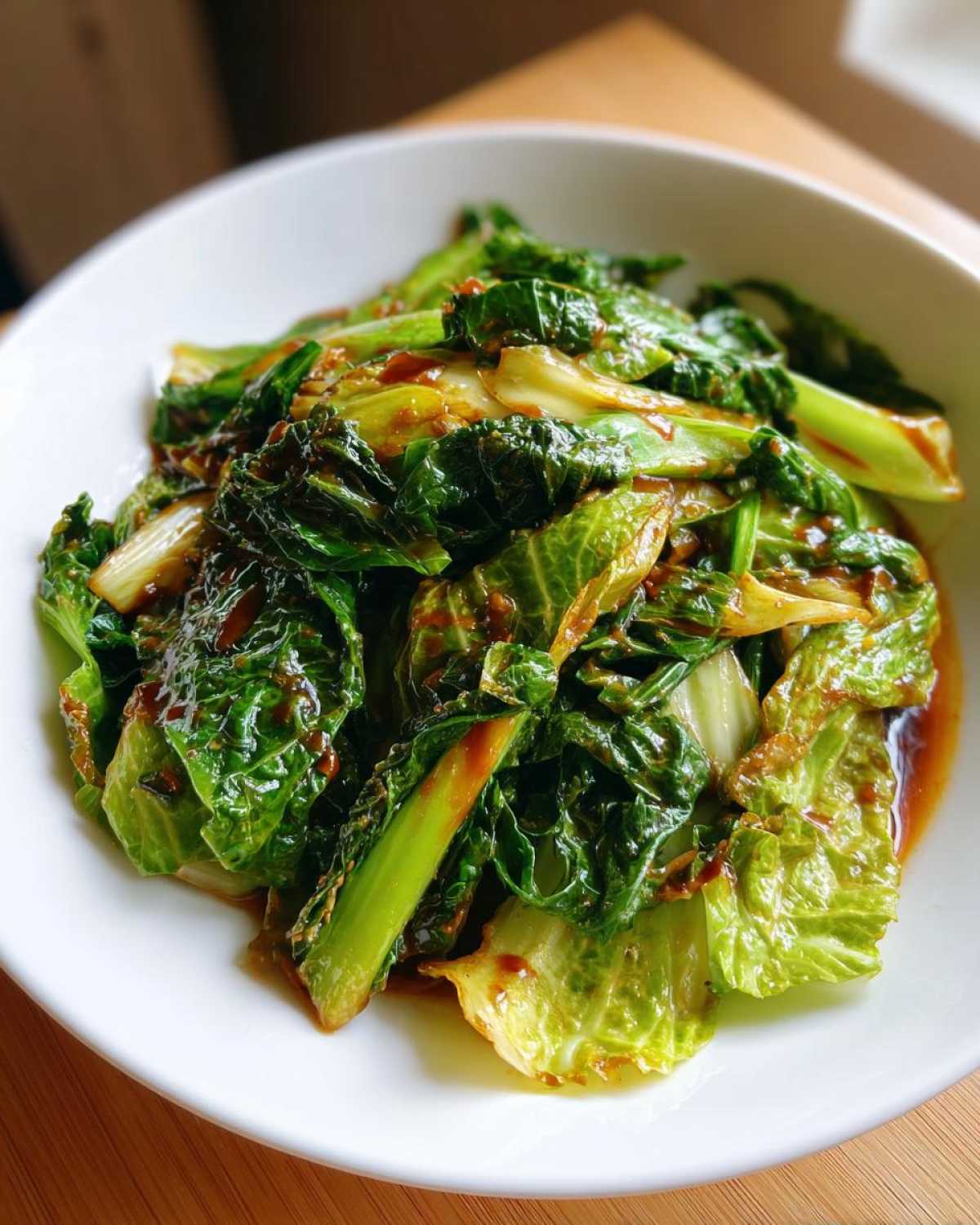 A close-up of vibrant green cabbage stir fry coated in a glossy garlic ginger sauce, served in a white bowl.