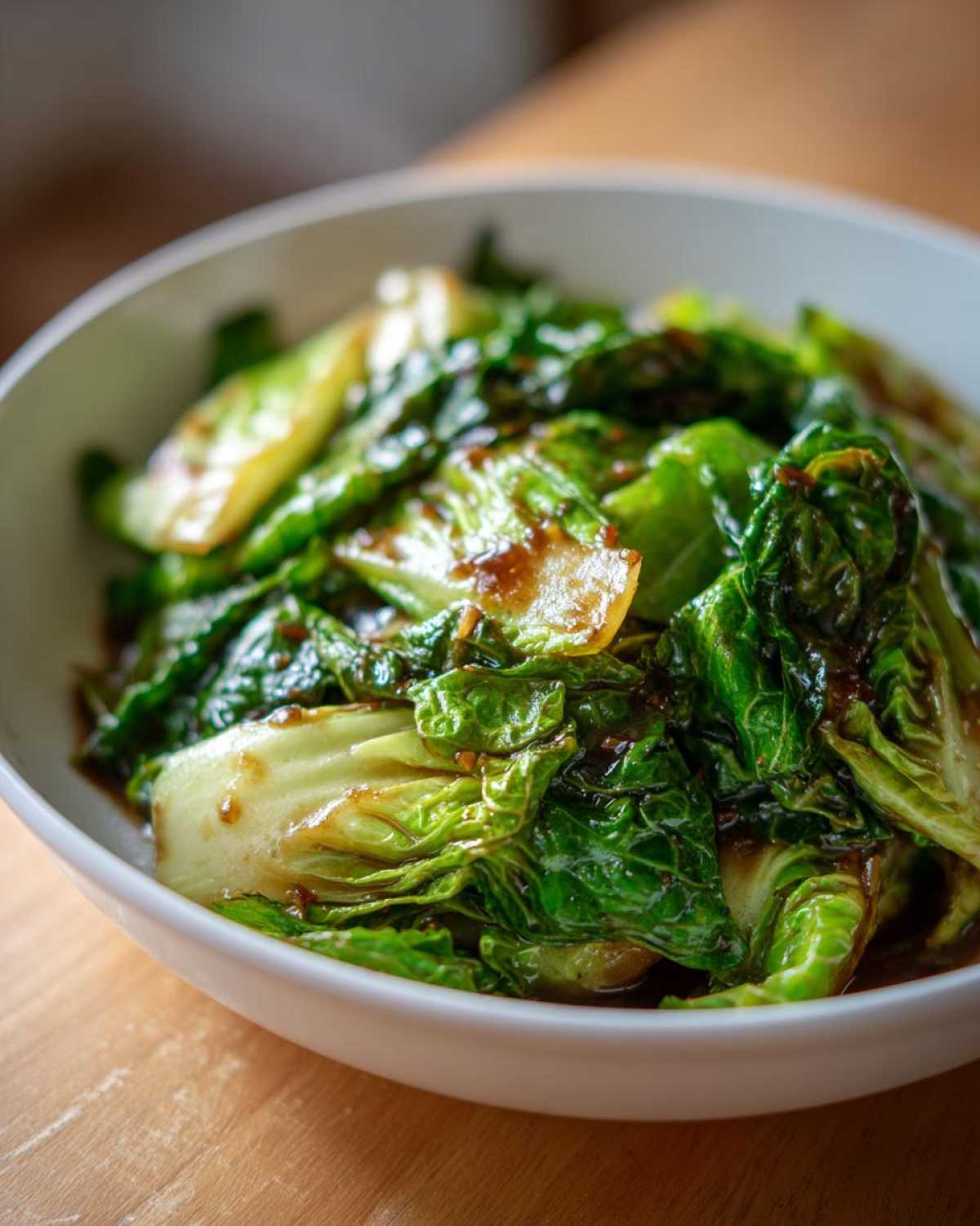 Close-up of vibrant green cabbage stir fry coated in a rich garlic ginger sauce, served in a white bowl.