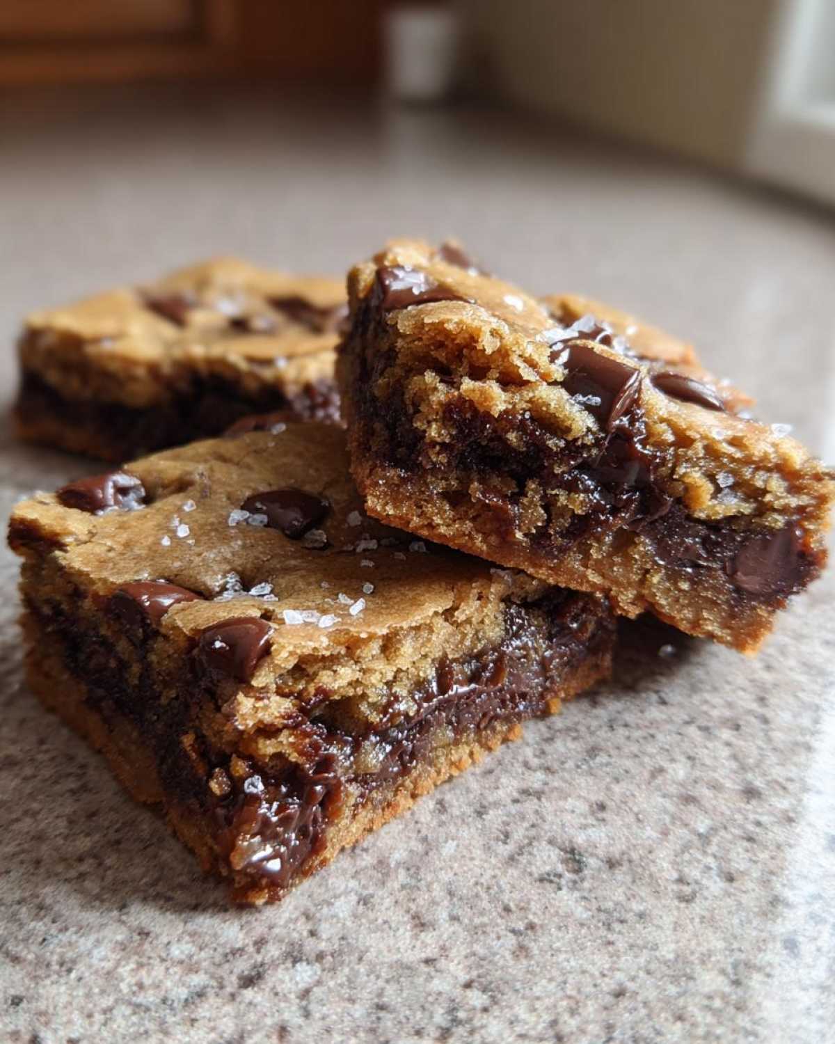 Close-up of three Chewy Chocolate Chip Cookie Bars stacked, showing gooey melted chocolate centers and flaky sea salt.