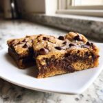 Two squares of Chewy Chocolate Chip Cookie Bars with gooey centers, topped with chocolate chips and sea salt.