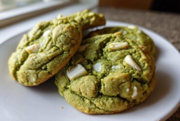 Close-up of three chewy matcha white chocolate cookies stacked slightly on a white plate.