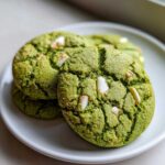 Close-up of several vibrant green Chewy Matcha White Chocolate Cookies stacked on a white plate.