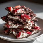 A stack of broken pieces of two-layer Chocolate Covered Strawberry Bark featuring dark chocolate, white filling, and sliced strawberries.