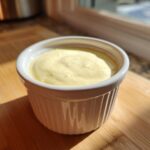 A small white ramekin filled with creamy yellow Copycat Taco Bell Chicken Quesadilla Sauce, sitting on a wooden board.