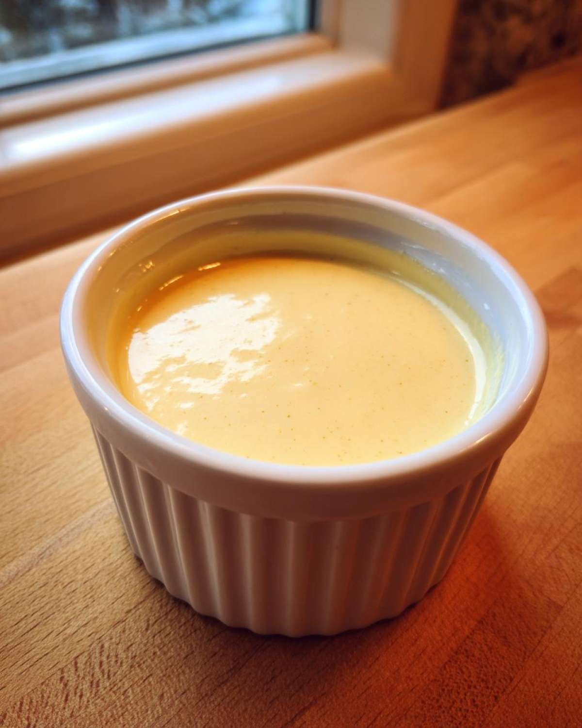 A small white ramekin filled with smooth, creamy yellow Copycat Taco Bell Chicken Quesadilla Sauce.