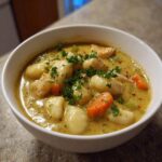 A close-up of a white bowl filled with rich, creamy Chicken Gnocchi Soup, featuring soft gnocchi, chicken pieces, carrots, and fresh parsley.