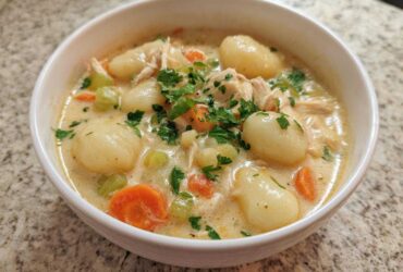 A close-up bowl of rich, creamy chicken gnocchi soup, featuring tender gnocchi, shredded chicken, carrots, celery, and fresh parsley garnish.