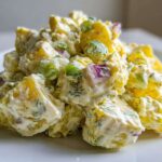 A close-up shot of a mound of Creamy Dill Potato Salad featuring yellow potatoes, red onion, green celery, and fresh dill.